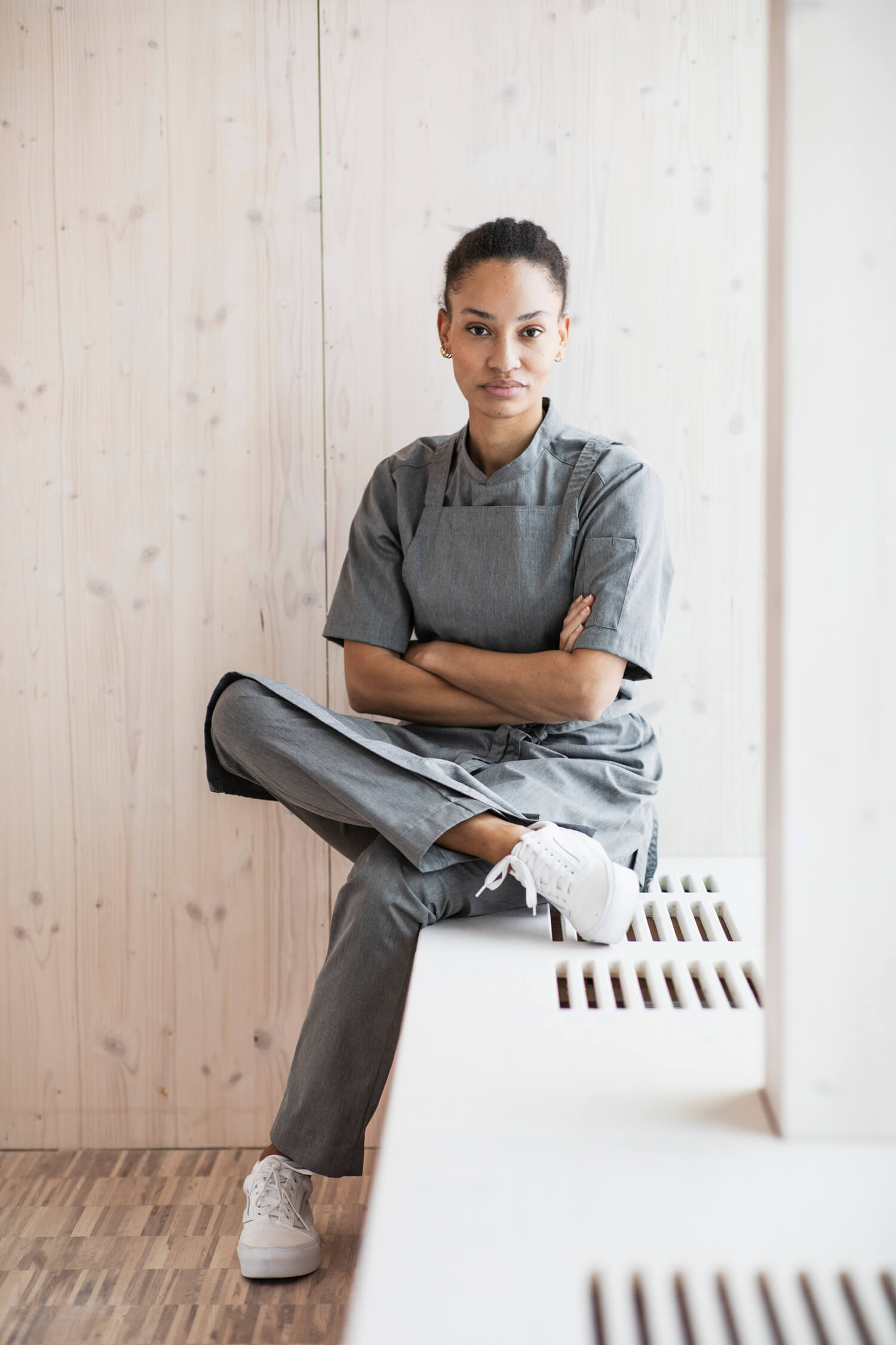 Kvinna i en modern och minimalistisk kök omgivning, klädd i Segers senaste nyheter - en stilren grå på grå uniform som speglar den nya tidens köksmode.