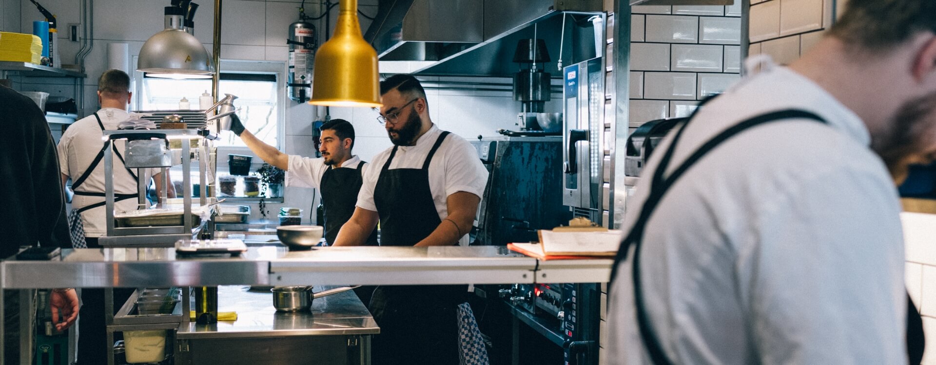 Kockar arbetar i restaurangkök med svarta förkläden och vita skjortor.