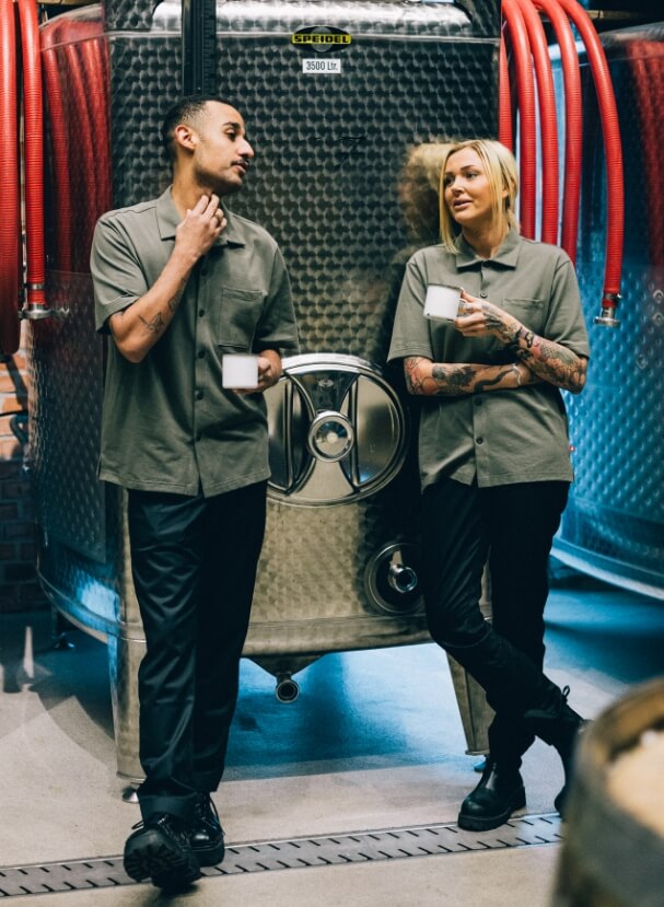 Två kollegor i restaurangbranschen lutar sig mot en stor tank och dricker kaffe i restaurangen. 